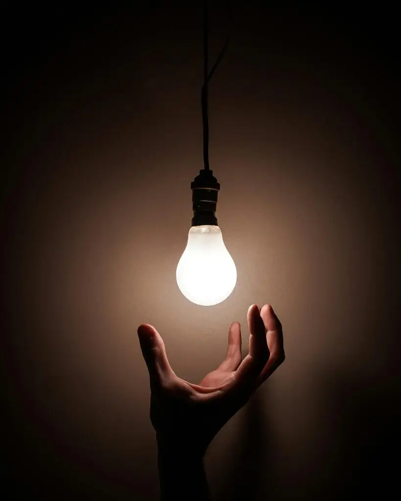 A hand reaching towards a glowing hanging light bulb symbolizing creativity and illumination.